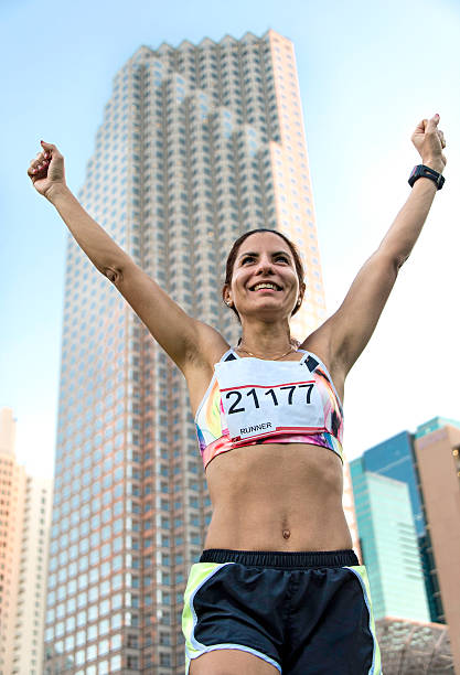 Hispanic Mature Runner Hispanic Mature female Runner smiling with her arms up after finishing an urban marathon miami marathon stock pictures, royalty-free photos & images