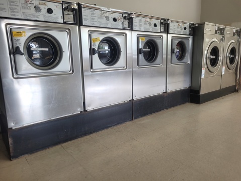 Stainless steel front loading washing machines are lined in a row at a laundromat.