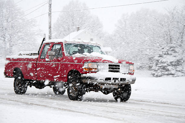 A 4x4 pickup truck driving down a snow covered road during a large winter storm.