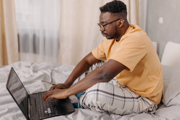 istock Young man utilizes laptop from the comfort of his bed, tackling tasks with efficiency 1554073813
