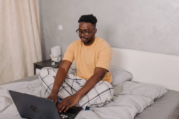 istock Young man stays connected and productive, utilizing his laptop in bed for morning tasks 1554073824
