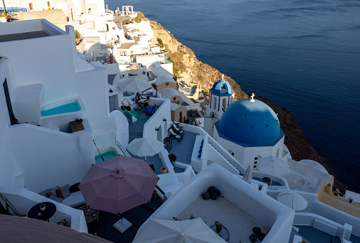 Oia, Santorini, Greece - June 28, 2021: View from viewpoint of Oia village with blue domes of  greek orthodox Christian churches and traditional whitewashed greek architecture.  Santorini, Greece