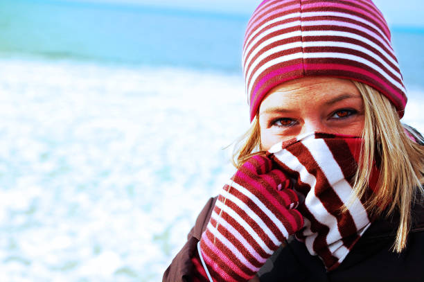 a close up shot of a girl bundled up in a winter hat, gloves and scarf outside against a snowy background. lively colors and stripes.