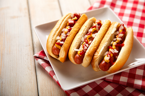 This is a photograph of three hot dogs on a white plate on a white wooden picnic bench. This is a great image for a Fourth of July picnic.