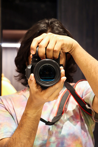 Stock photo showing close-up view portrait of male photographer looking at camera whilst holding a digital SLR camera to take his own photograph.