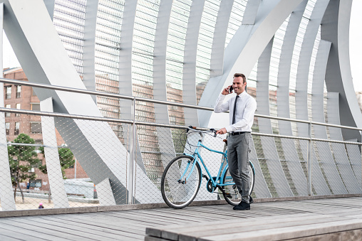 Business man standing in a bridge with his vintage bicycle speaking on the mobile phone