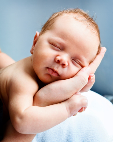 Close up of smiling caucasian hairy brunet cute newborn baby sleeping.One or two week child in male hands.Unrecognizable man, father,holding child.Care,love,happiness concept.