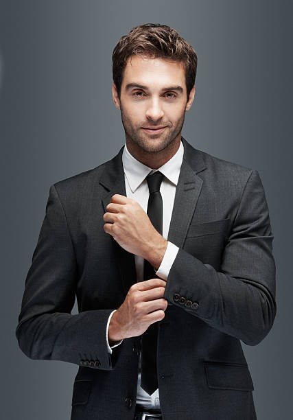 For the man who has it all Gorgeous young man doing up his cufflinks and looking at you, isolated on grey - copyspace urbane stock pictures, royalty-free photos & images