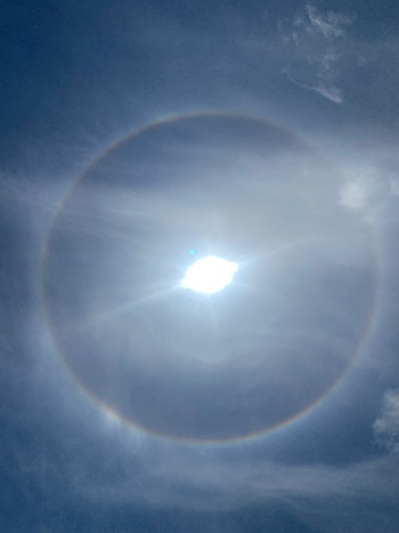 A halo  is an optical phenomenon produced by light (sun) interacting with ice crystals suspended in the atmosphere.