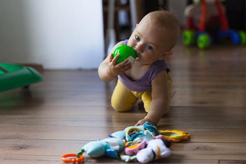 Curious baby in motion, crawling with a green ball in hand, exploring by tasting