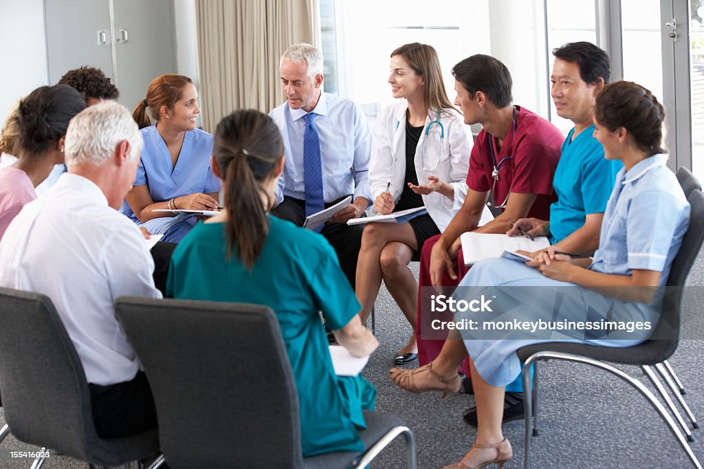 Medical Staff Seated In Circle At Case Meeting Medical Staff Seated In Circle Talking At Case Meeting. Doctor Stock Photo