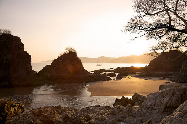The sun rises over the mountains behind Sayulita Mexico and reflects off the ocean. A sailboat is moored in the bay. Sayulita is an old fishing village near Puerto Vallarta. Shot into sun with resulting lens flare.