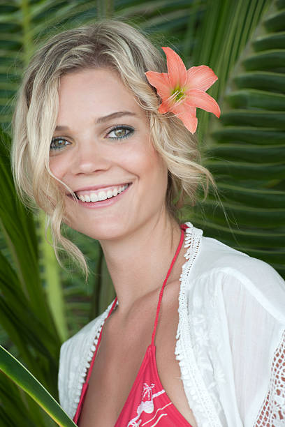 Pleased asian half-naked lady with lily flower in head looking camera and smiling isolated over white