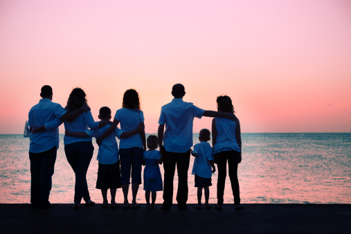 Silhouetted family of 8 watching the sun setting over the ocean.