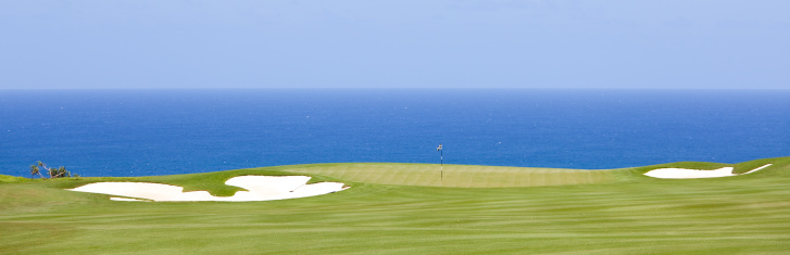 A beautiful golf course by the ocean. White sand bunkers. Kauai, Hawaii, United States. Golf scenic. Horizon over water. Horizontal colour image. Copyspace and blue sky. Panorama. This golf image shows the dramatic beauty of golfing in the tropical zone and, specifically, Hawaii. Kauai is one of the golfing hot spots in the state of Hawaii. 