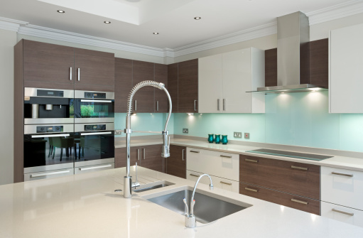 a section of a lovely kitchen in a modern new home featuring a large kitchen island in the foreground. A large extentable kitchen tap sits by a sink on the island whilst to the right is a 