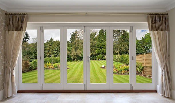 beautiful concertina doors with garden view a set of concertina patio doors with silk curtains on either side and a view of a fabulous garden. A large nicely mowed lawn stretches away towards a backdrop of mixed trees. curtain rail stock pictures, royalty-free photos & images