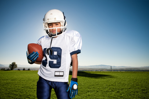 Dramatic portrait of a young hispanic boy wearing his football uniform on the field.