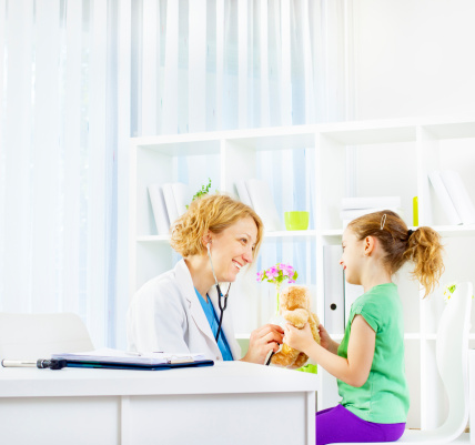 Cute little girl with teddy bear at doctors office, female doctor listening to heartbeat of teddy bear getting friendly with smiling little girl. can be used as how to eliminate fear of doctors or similar.