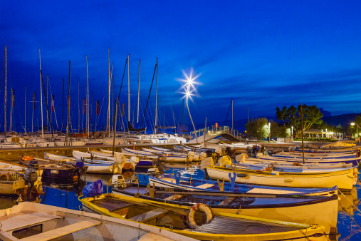 People enjoying a mild spring evening at the colorful harbor of Bardolino, where traditional fishing boats are moored. Bardolino is one of the attractive cities on the Veronese shores of Lake Garda, the largest Italian lake and a major tourist destination.