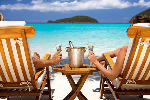 couple en lune de miel dans des fauteuils inclinables boire du champagne sur une plage des caraïbes - mer des caraïbes photos et images de collection