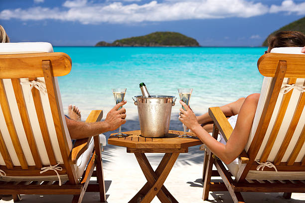 honeymoon couple in recliners drinking champagne at a Caribbean beach honeymoon couple sitting in luxury recliners at a tropical Caribbean beach resort and celebrating with a champagne caribbean islands stock pictures, royalty-free photos & images
