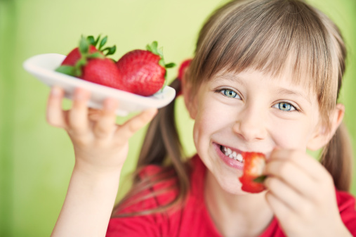 Smiling little girl eating strawberries.