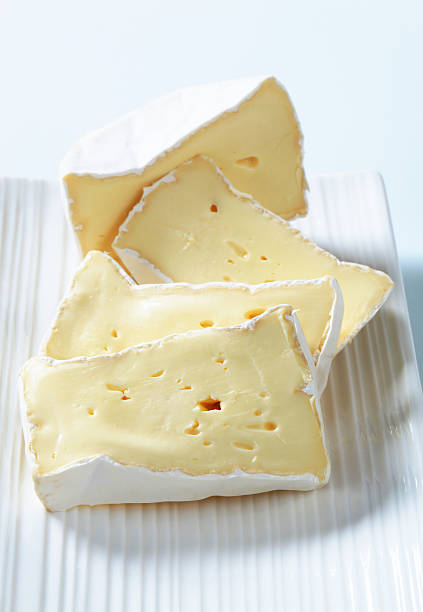 Close up of soft French Brie cheese pieces on wooden board on dark background. Cheeseboard of Three pieces of cheese