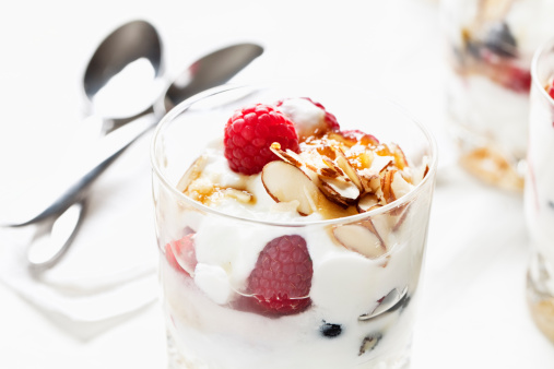 raspberries and yoghurt in a glass, sweetened with honey, decorated with sliced almonds 