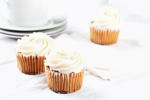 carrot cupecakes with vanilla icing on white table cloth, white cups in background