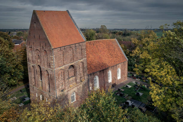 Suurhusen, Germany - October 27, 2022: Aerial view of the “Leaning Church Tower of Suurhusen” in autumn. In the municipality of Hinte is the church tower of Suurhusen, which is 27.37 meters high and has a cantilever of 2.47 meters. That corresponds to an incline of 5.19 degrees.