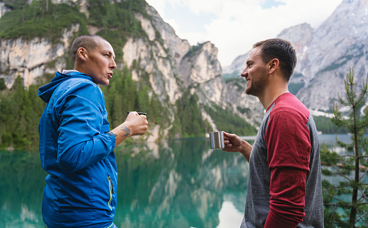 Caucasian male hikers having a drink from a travel mug, in front of the Lake Prags/Braise