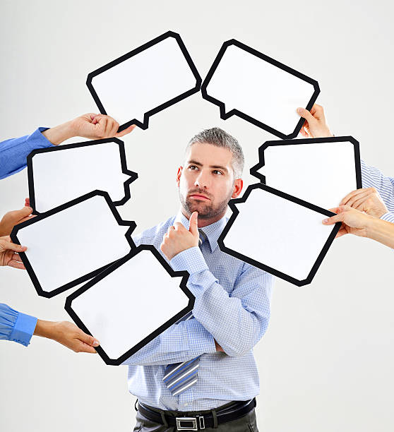 Difficult choice Portrait of serious businessman surrounded by many speech bubbles with copyspace. business person one man only blue standing stock pictures, royalty-free photos & images