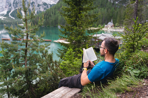 Young Caucasian man sitting on the bench near the Lake Prags/Braise, and reading a book