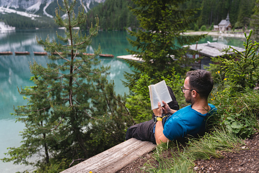 Young Caucasian man sitting on the bench near the Lake Prags/Braise, and reading a book