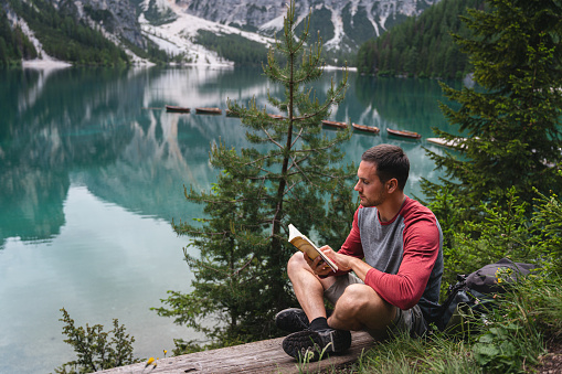 Young Caucasian man sitting on the bench near the Lake Prags/Braise, and reading a book