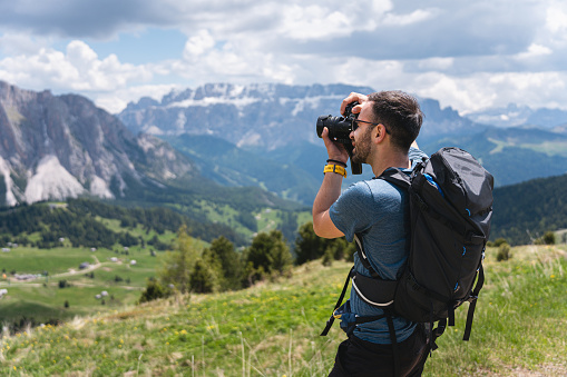 A young male Caucasian hiker, with a camera taking photos of the Alpe di Seceda