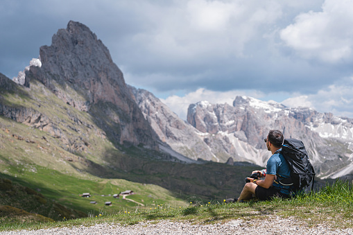 Caucasian man, taking a break from hiking while admiring the view of Alpe di Seceda
