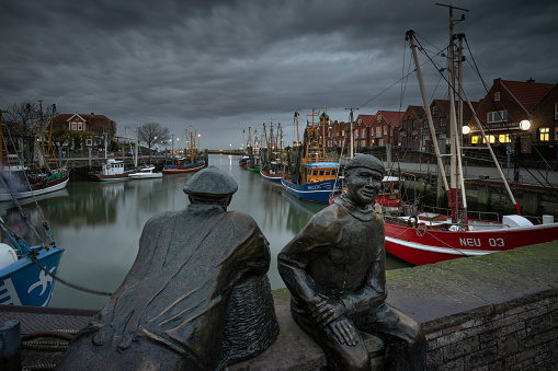 Neuharlingersiel, Germany - October 27, 2022: Two sculptures - old fisherman and young fisherman - have found their place on the harbor wall since the year 2000. The Esens artist Hans-Christian Petersen, created the group of sculptures together with his brother Anders, based on a drawing from the 1920s by the artist Jeanne Mammen.
