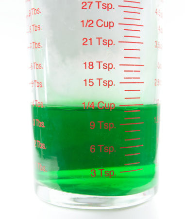 1/4 cup of a green liquid in a small plastic measuring container. On a white background.