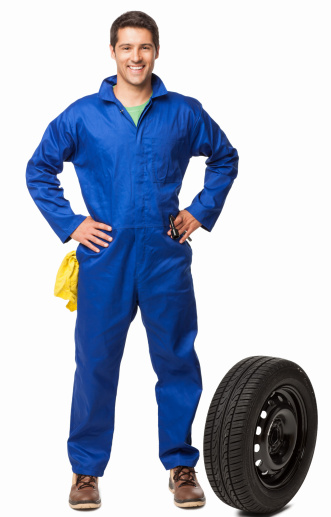 Full length portrait of an automotive technician with a spare tire. Vertical shot. Isolated on white.