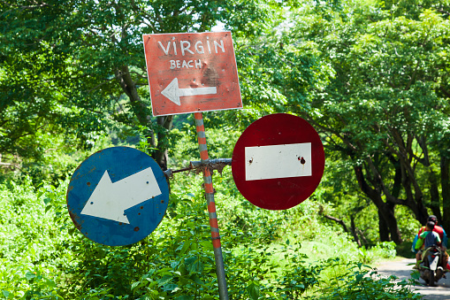March 15, 2022 - Virgin Beach, Karangasem Regency, Bali, Indonesia.\nA set of road signs on a single sign post with a red no entry sign for going straight, a blue keep left sign, and a hand painted red and white sign pointing to Virgin Beach in Karangasem Regency in Bali. Virgin beach also known as White Sand Beach is one of Bali's most beautiful beaches.