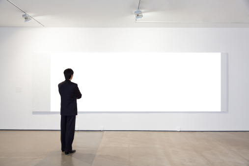 Businessman looking at white frames in an art gallery