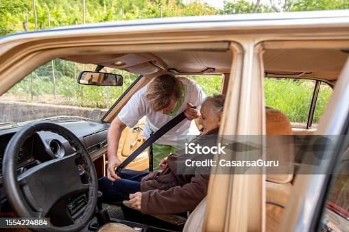 istock Caregiver helping a senior woman with a seat belt in a car 1554224884