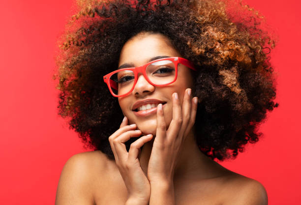 Portrait of Young African model wearing eyeglasses over red color background Portrait of Young African female model wearing eyeglasses over red color background teenage girl before and after make up stock pictures, royalty-free photos & images