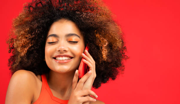 Portrait of an excited young afro american woman talking on mobile phone Portrait of an excited young afro american woman talking on mobile phone over red background. teenage girl before and after make up stock pictures, royalty-free photos & images