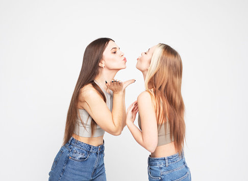 Two cheerful young female friends laugh and rejoice, have fun together. Girls with long hair, beautiful, young, charming, posing over white background. Lifestyle concept.