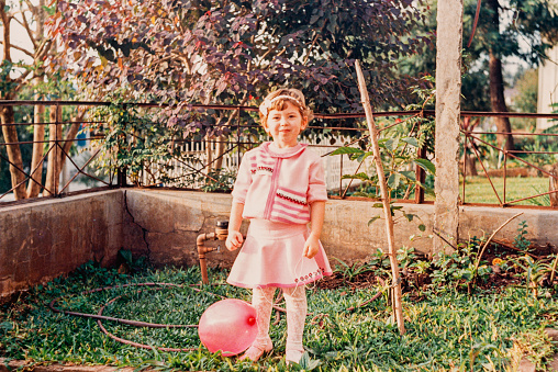 Vintage portrait of a girl in the backyard of her house looking at the camera holding a wire stuck in a bladder in the 90s in Brazil.