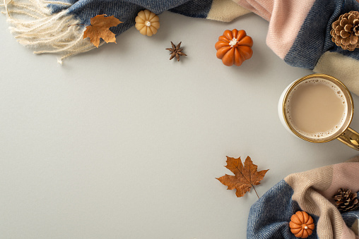 Cozy fall vibes at home: High angle view of a warm patchy blanket, maple leaves, pumpkin candles and aromatic spices with ample space for text or advertising on a light grey isolated background