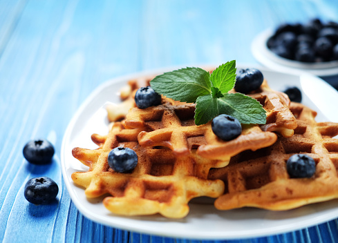 Waffles with blueberries and raspberries for breakfast on white plate over blue wooden table. Close up.